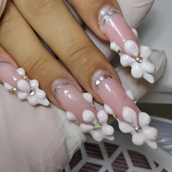 Unhas longas em nude rosado com flores brancas em 3D e strass