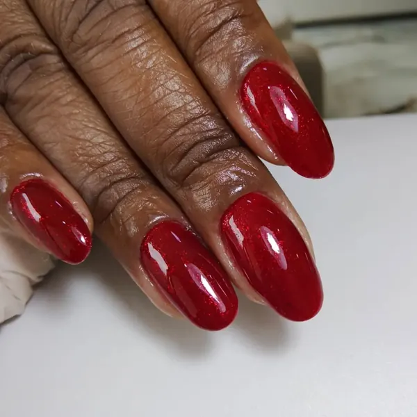 Unhas amendoadas em vermelho com glitter fino, em mão de pele negra